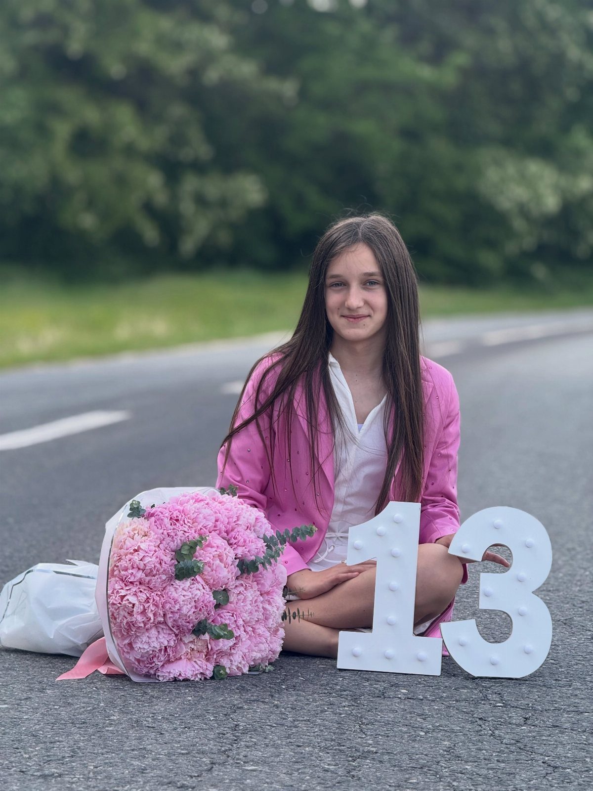 Teenage girl in pink blazer sitting on road with pink flowers and number 13