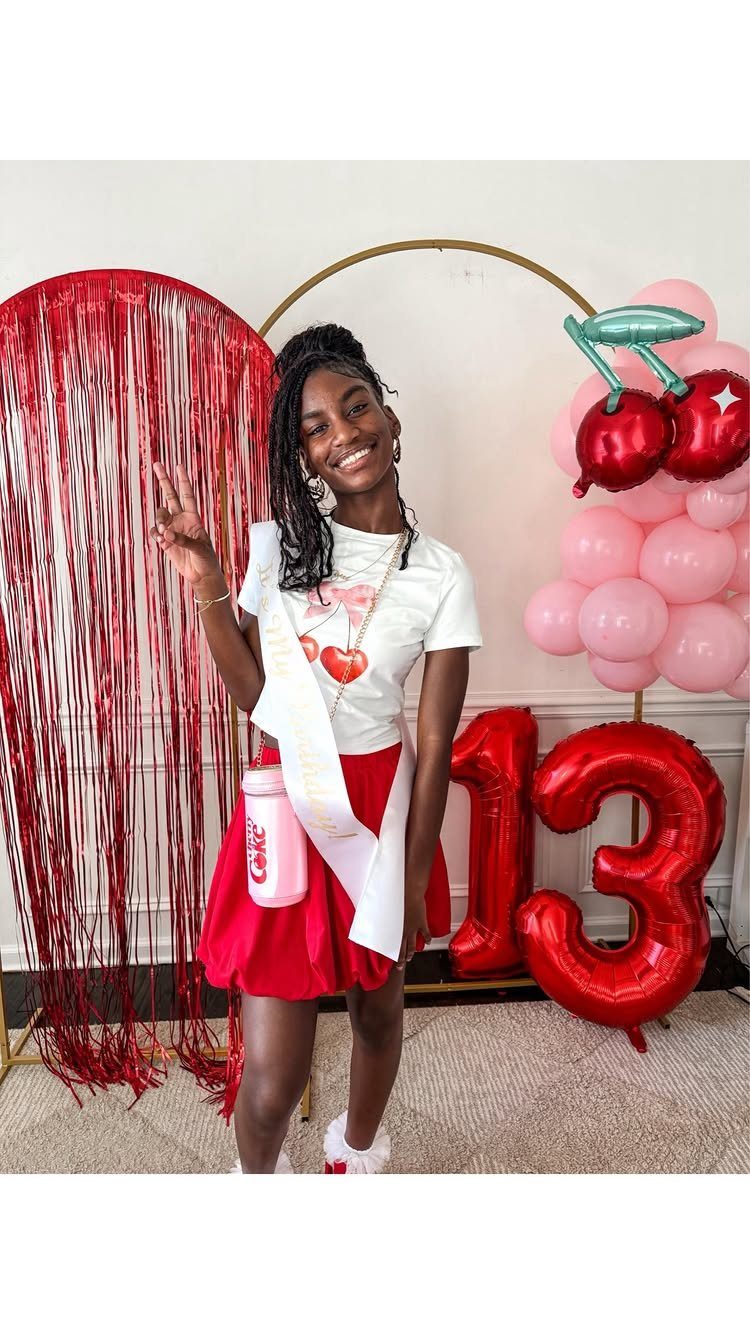 Teenage girl in white t-shirt and red skirt posing by 13th birthday decorations