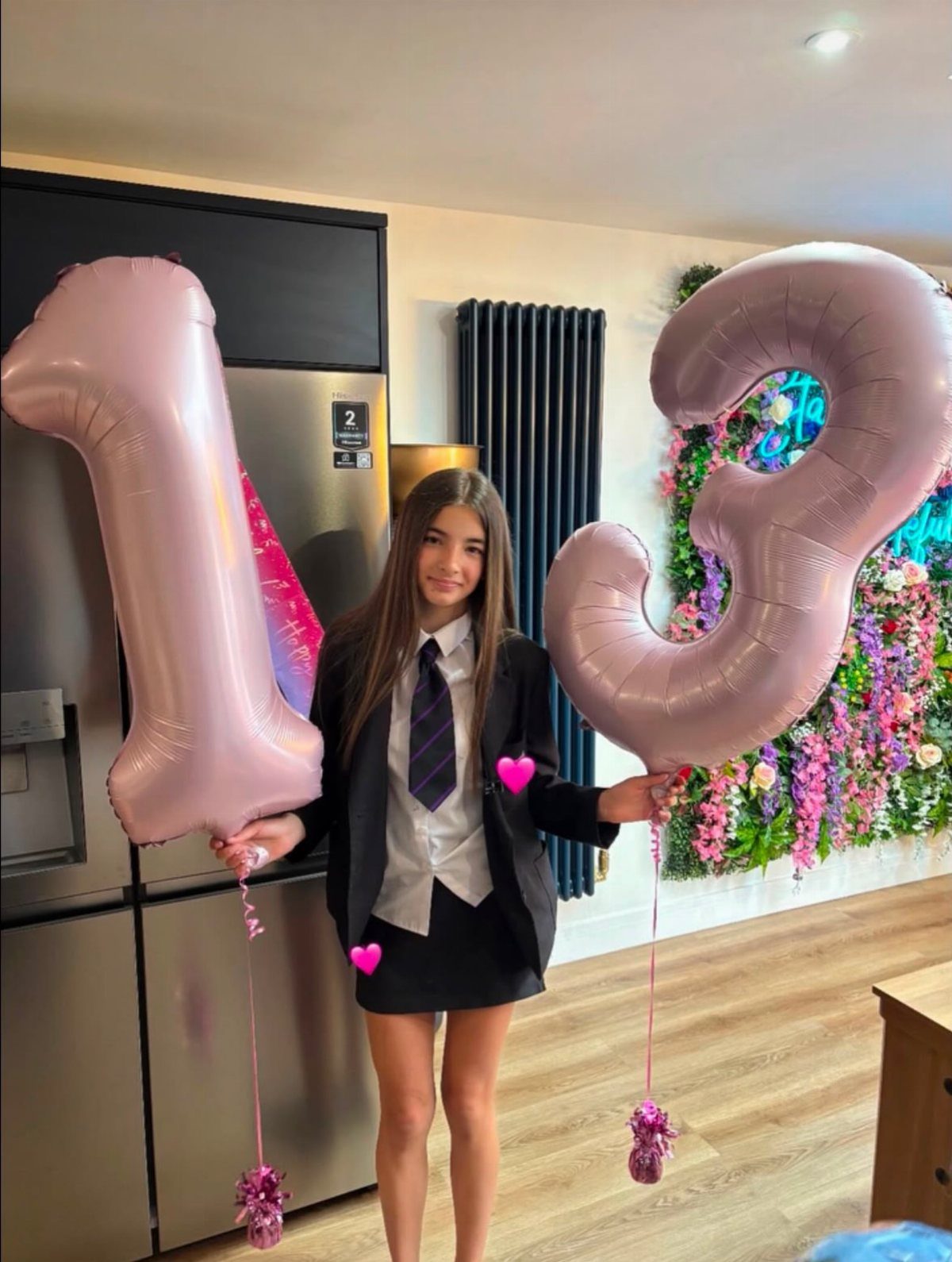 Teenage girl holding pink number 13 balloons wearing a black blazer and skirt