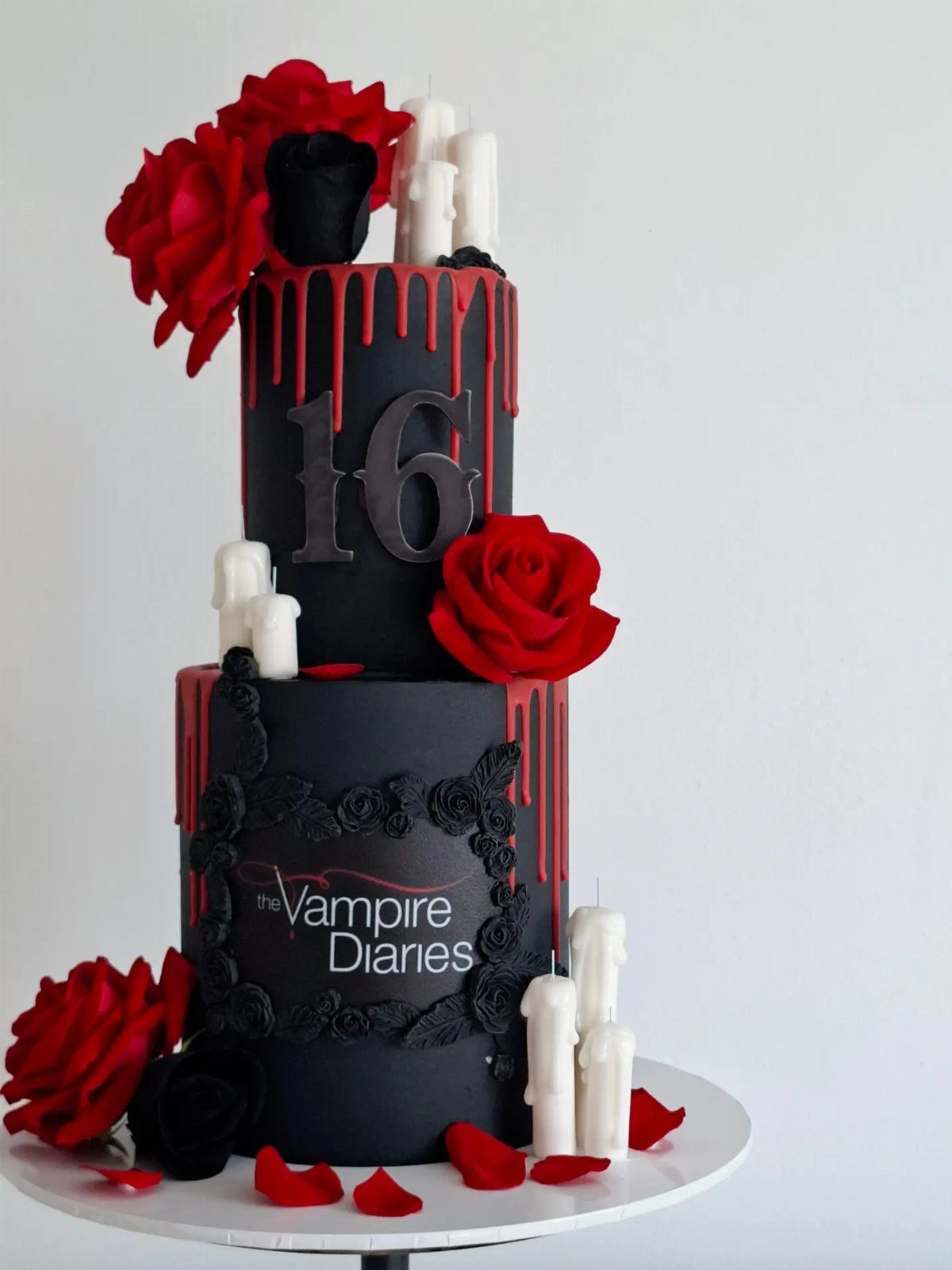 Two-tier black and red gothic cake with roses, candles, and number 16.