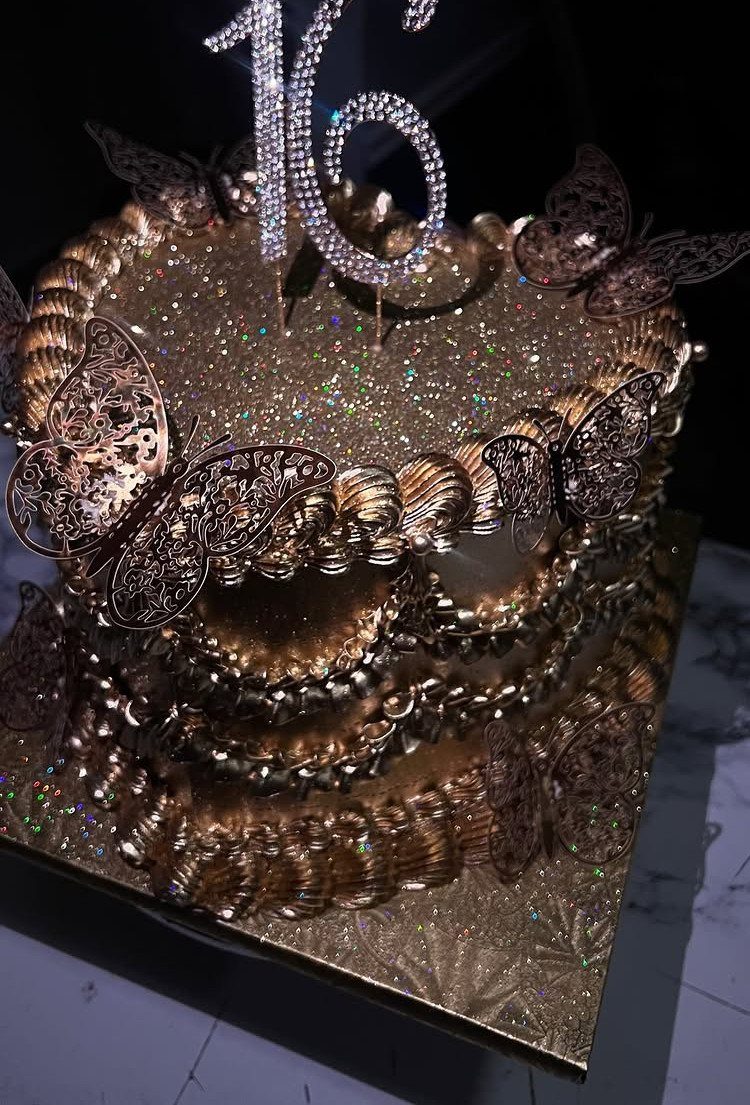 Gold glittery two-tier cake with butterfly decorations and a sparkling 16 topper.