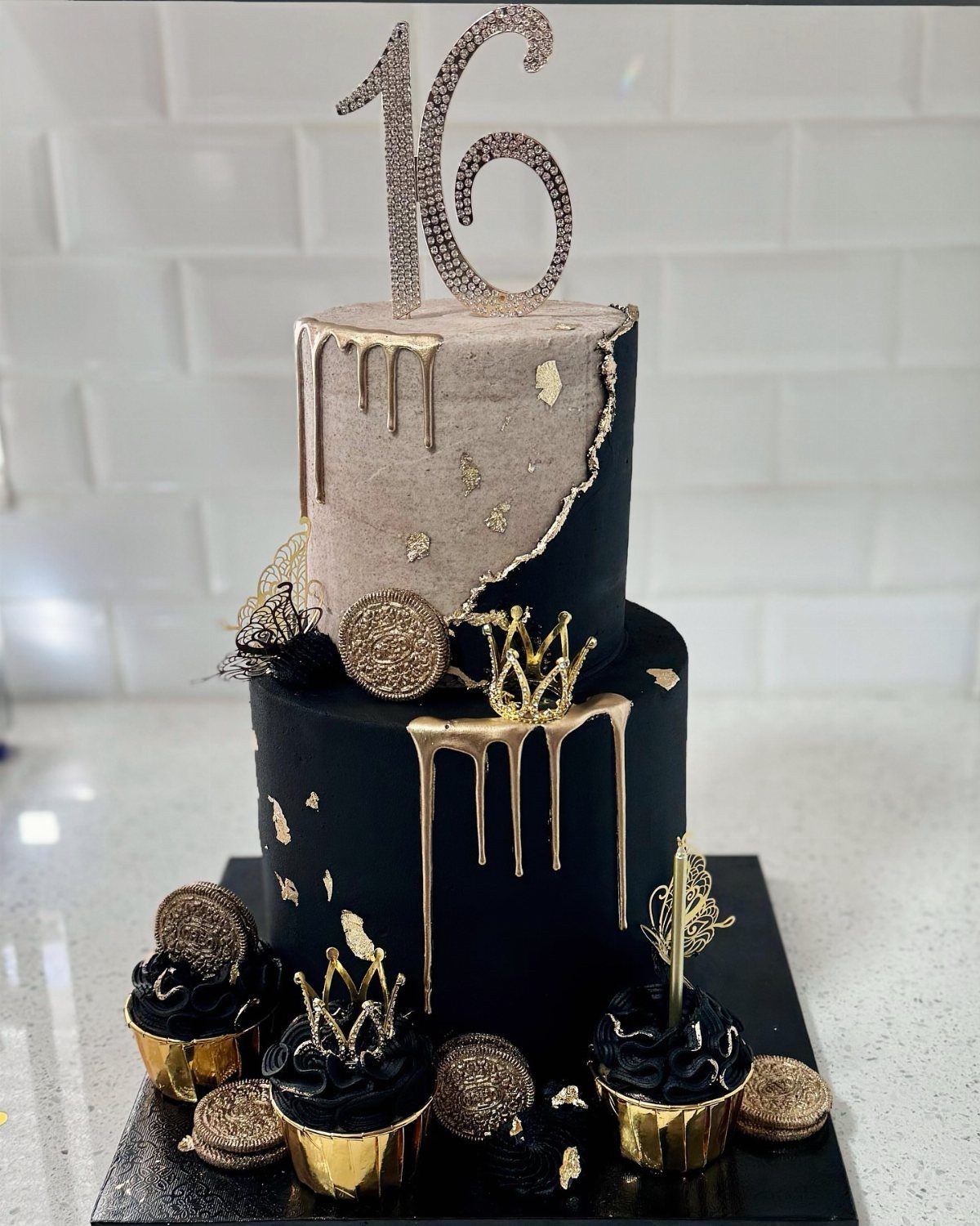 Two-tier black and champagne cake with gold drips and a glittery 16 topper.
