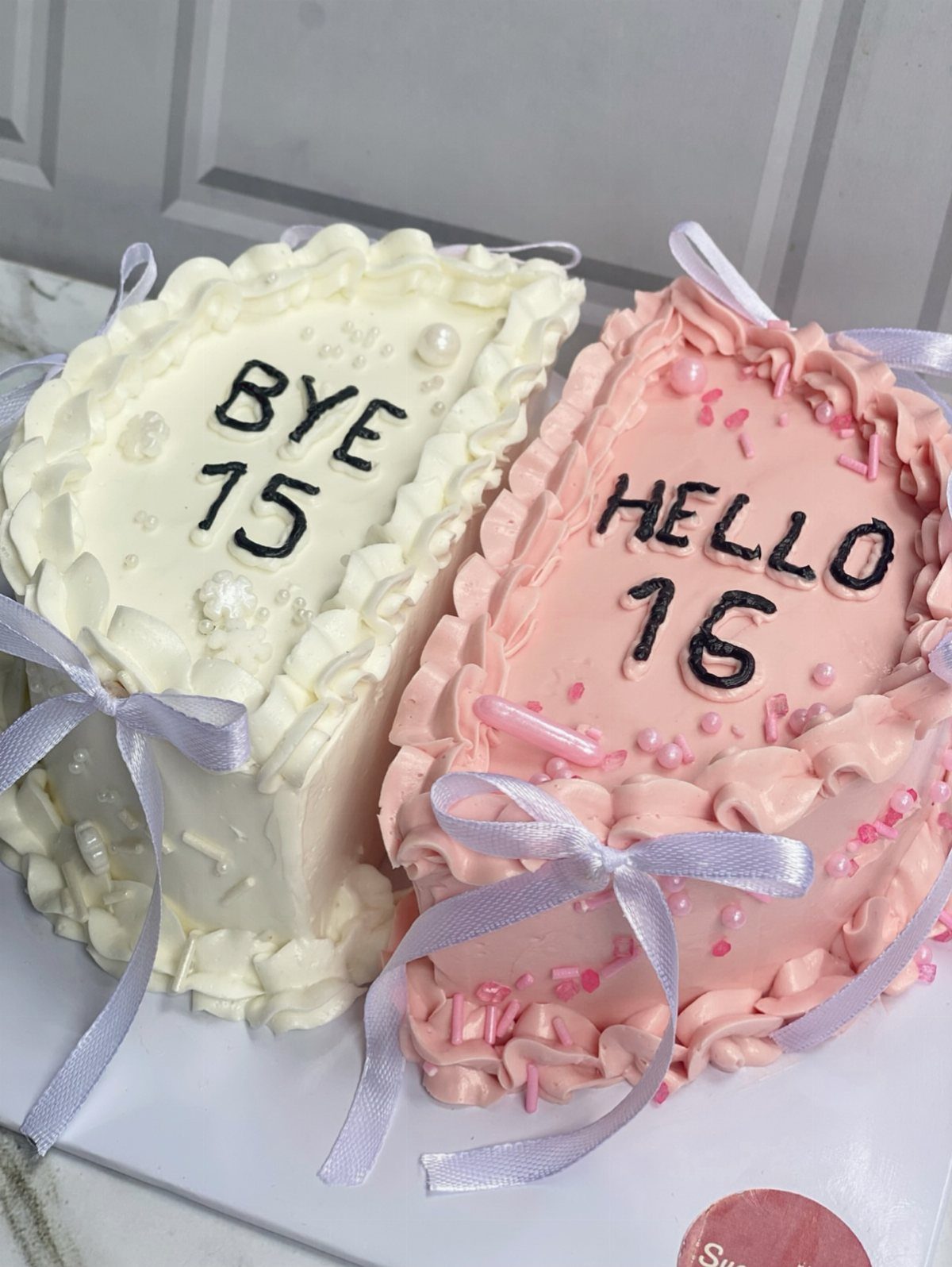 Two heart-shaped cakes, white and pink, reading BYE 15 and HELLO 16.