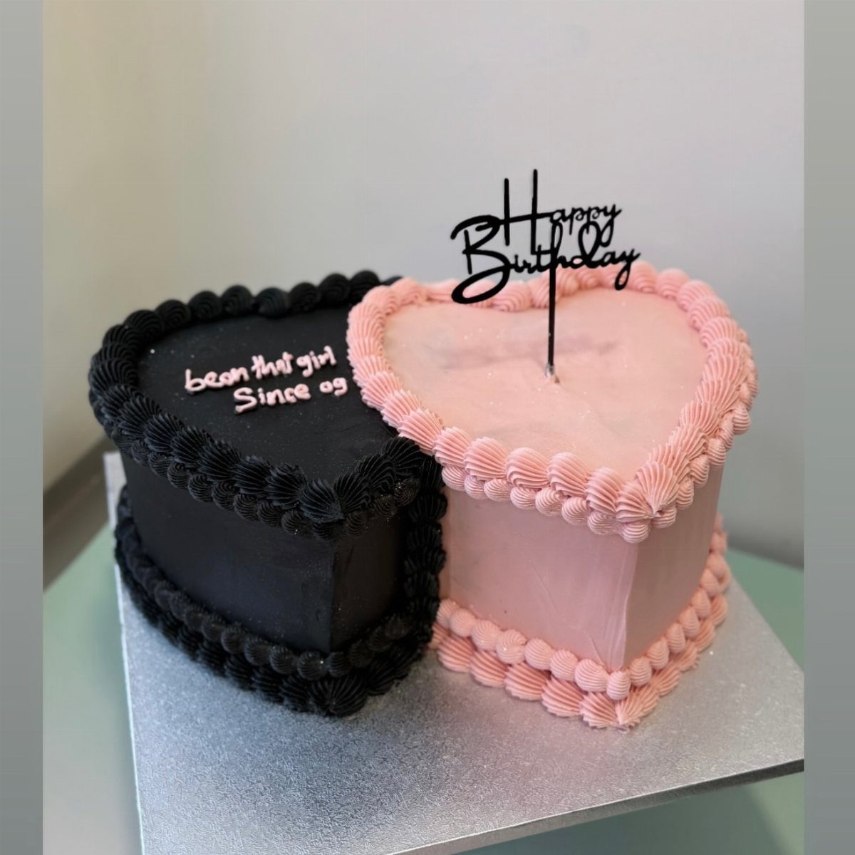 Two heart-shaped birthday cakes in black and pink with a Happy Birthday topper.