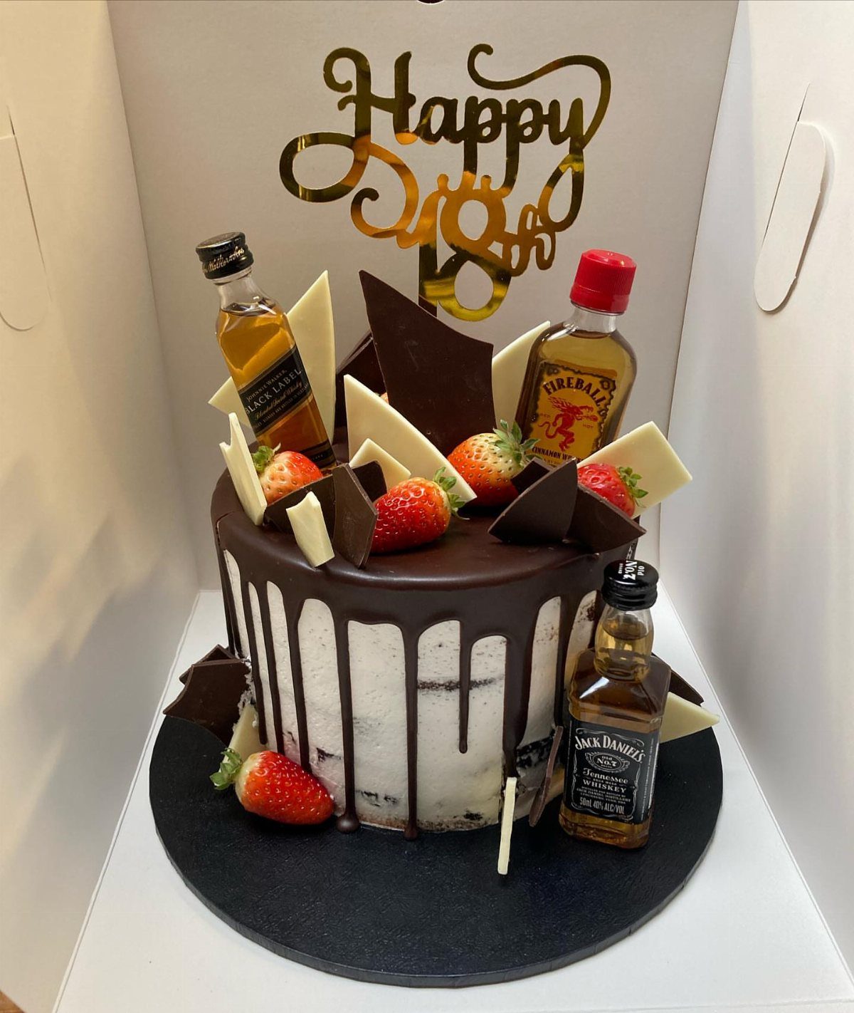 White cake with chocolate drip, strawberries, mini liquor bottles, and gold 18th topper.