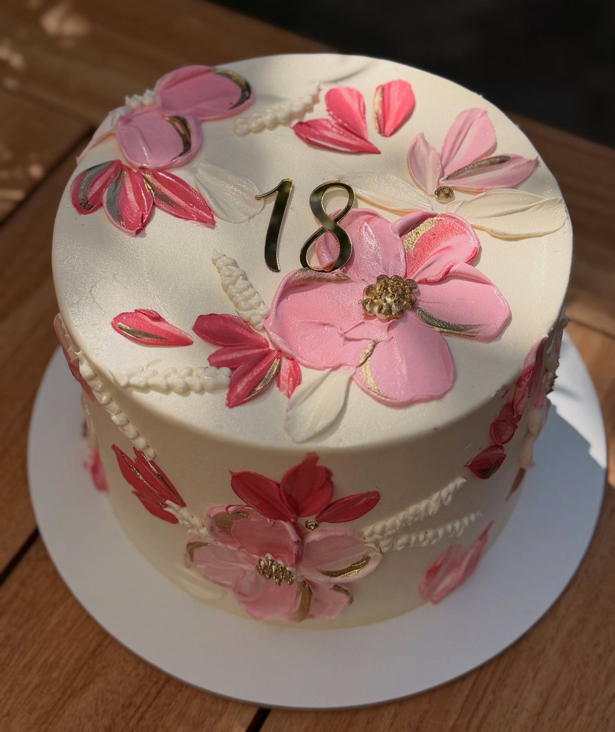 White birthday cake with pink buttercream flowers and a gold number 18 topper.