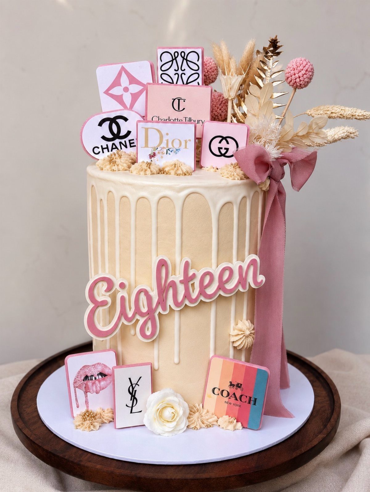 Cream drip cake for an 18th birthday decorated with luxury brand logo toppers.
