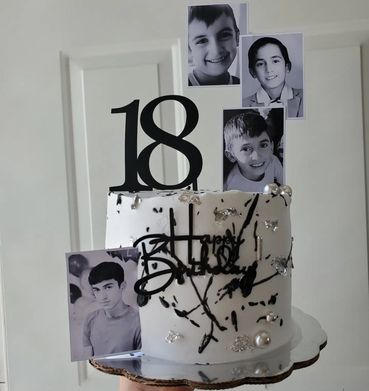 White birthday cake with black splatters, number 18 topper, and personal black-and-white photos.