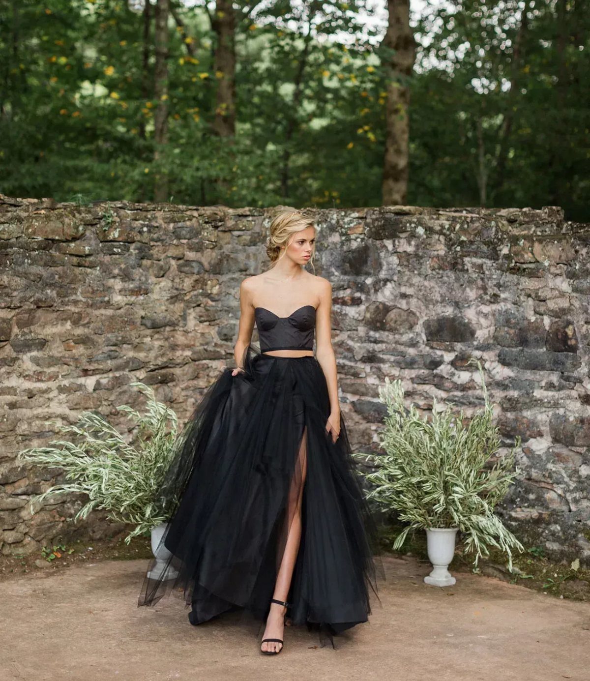 Woman in a black corset top and tulle skirt posing by a stone wall