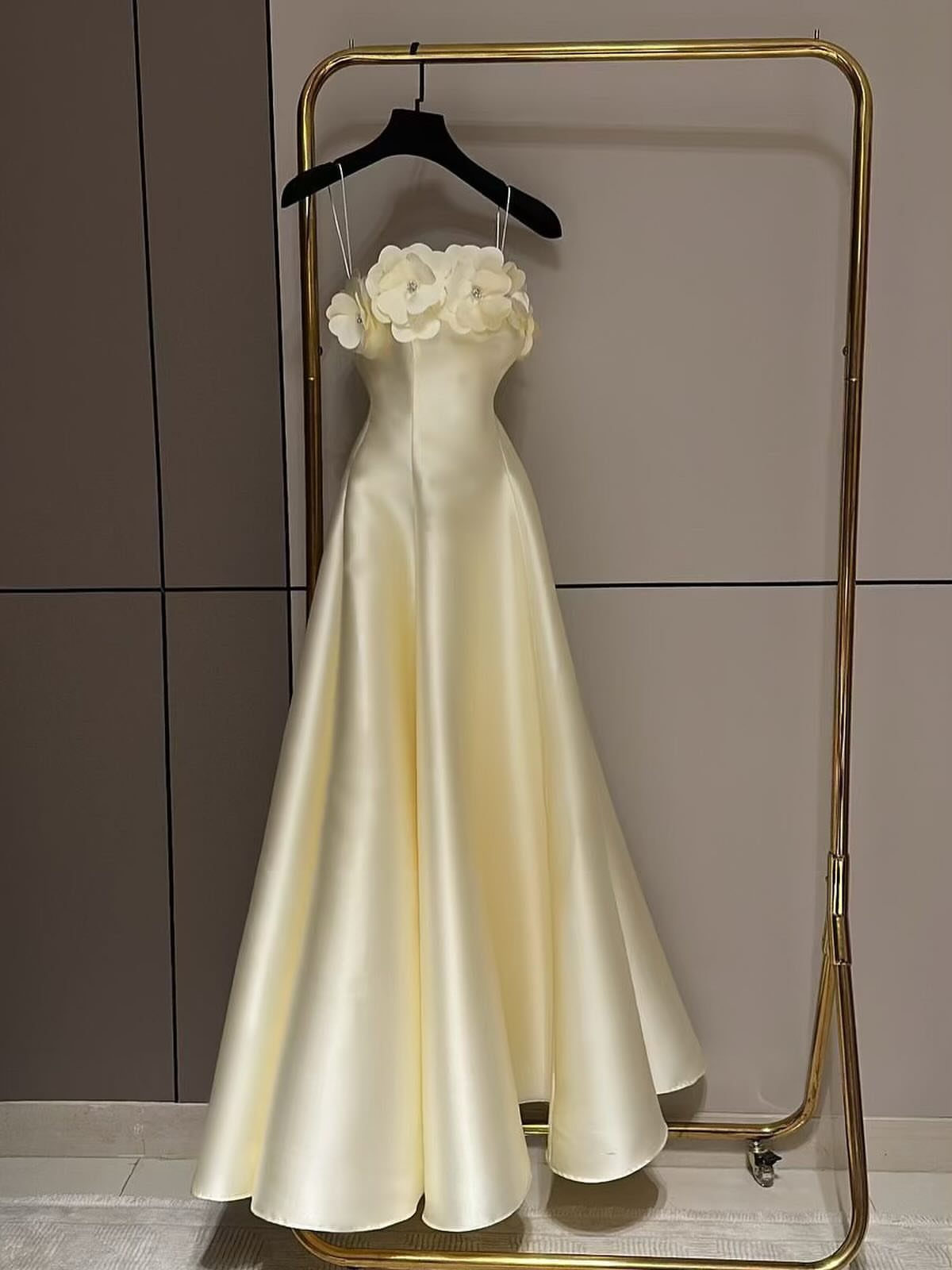 Cream-colored floor-length satin gown with floral bodice hanging on a gold rack