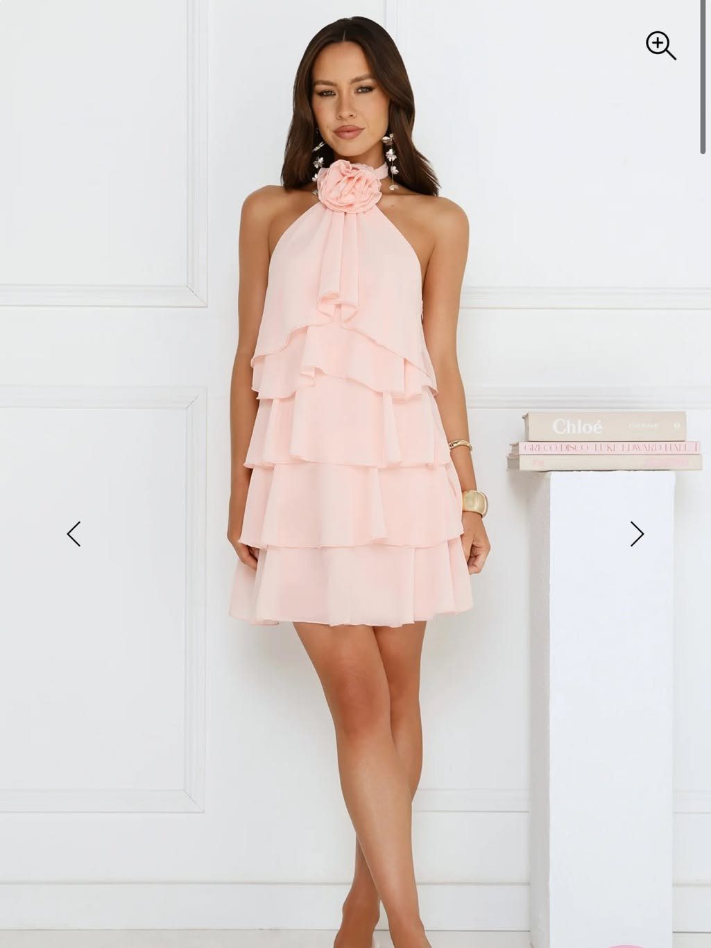 Woman wearing a light pink tiered chiffon halter-neck mini dress against white walls