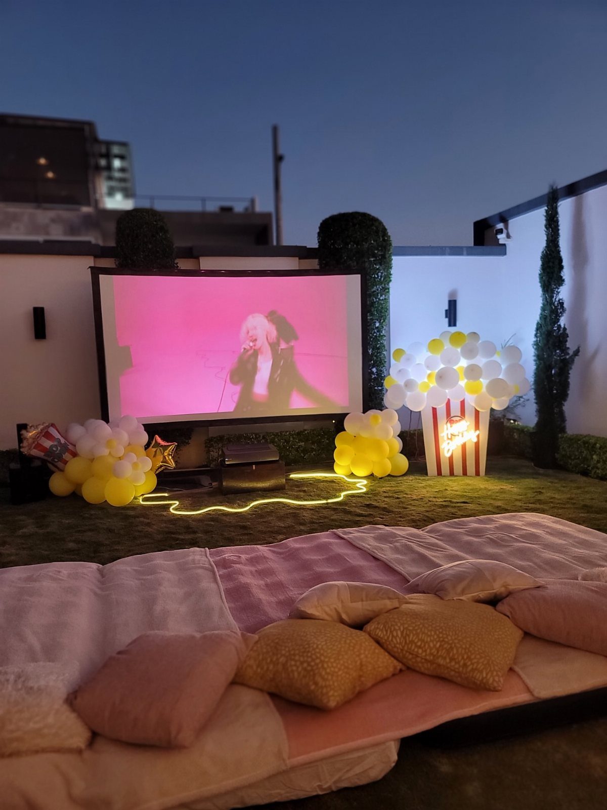 Outdoor movie setup with a projector screen, balloons, and cozy floor seating.