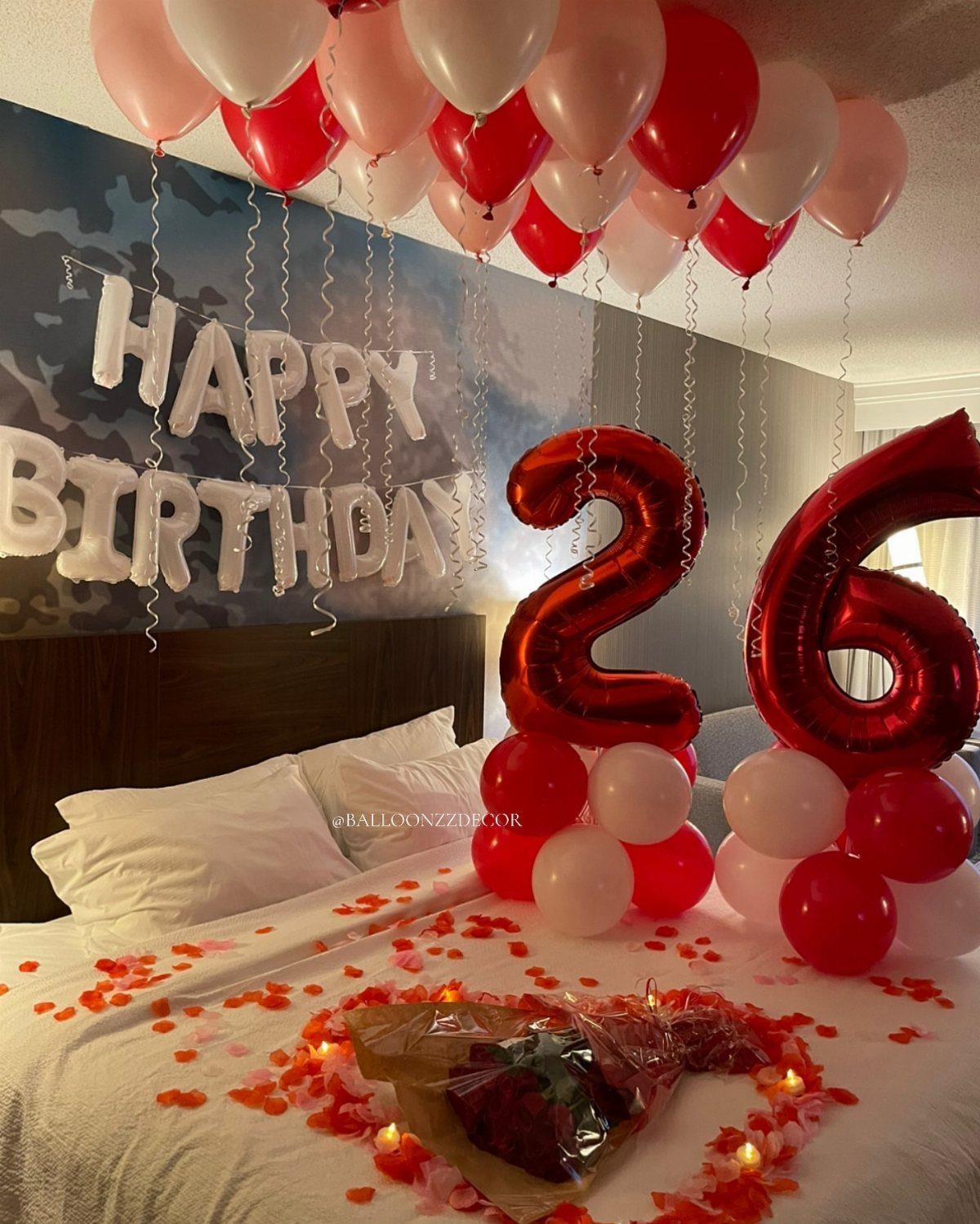 Bed decorated with red and white balloons, rose petals, and 26th birthday signage.