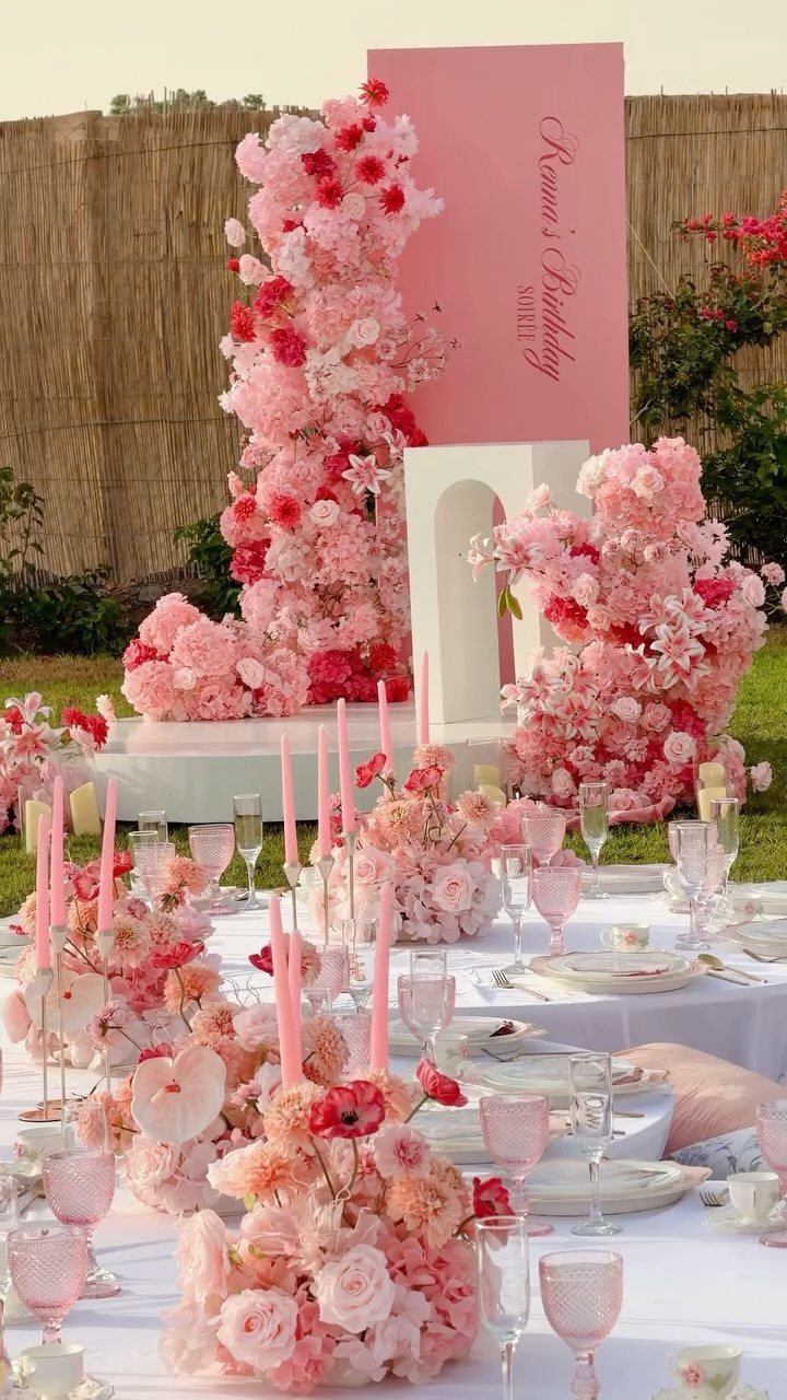 Outdoor birthday table with pink floral centerpieces, pink candles, and large flower walls.