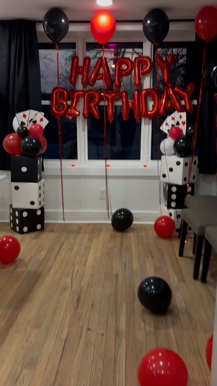 Birthday party decorations featuring red and black balloons, giant dice, and playing cards.