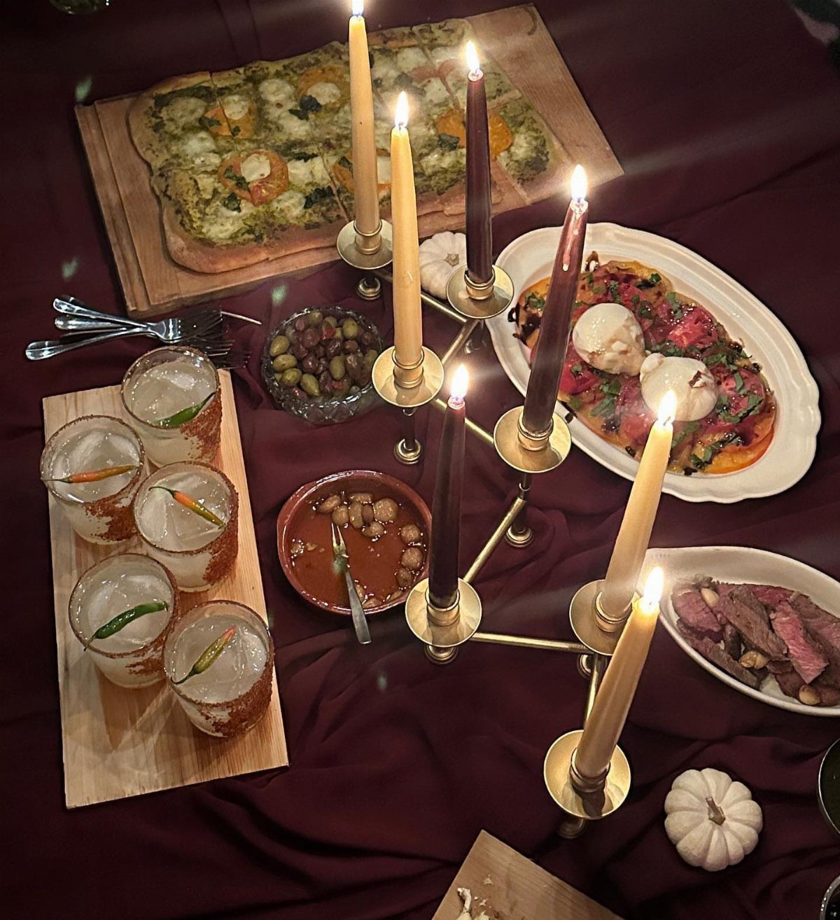 Dinner table with burgundy cloth, lit candles, cocktails, and various gourmet appetizers.