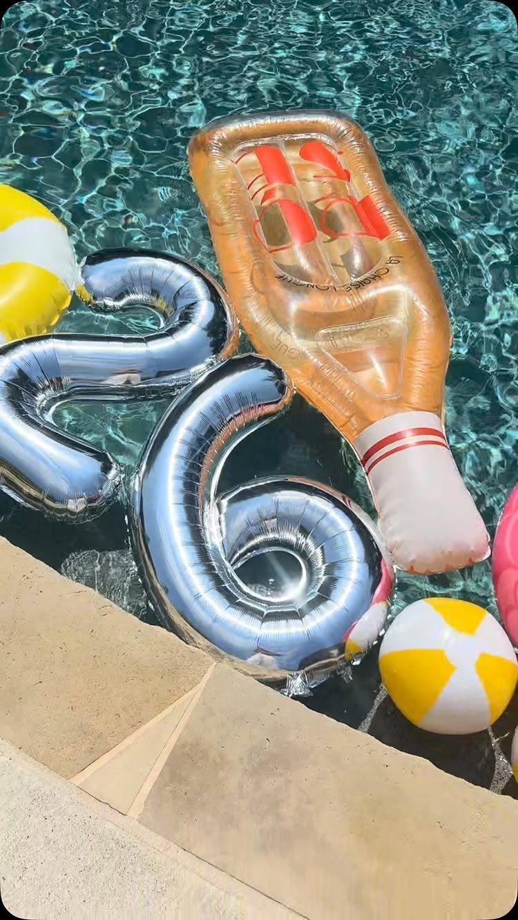 Silver number 26 balloons and champagne float floating in a blue swimming pool.