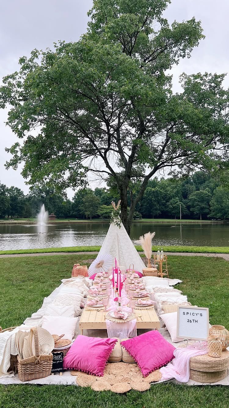 Upscale picnic setup with pink decor and a teepee by a scenic lake.