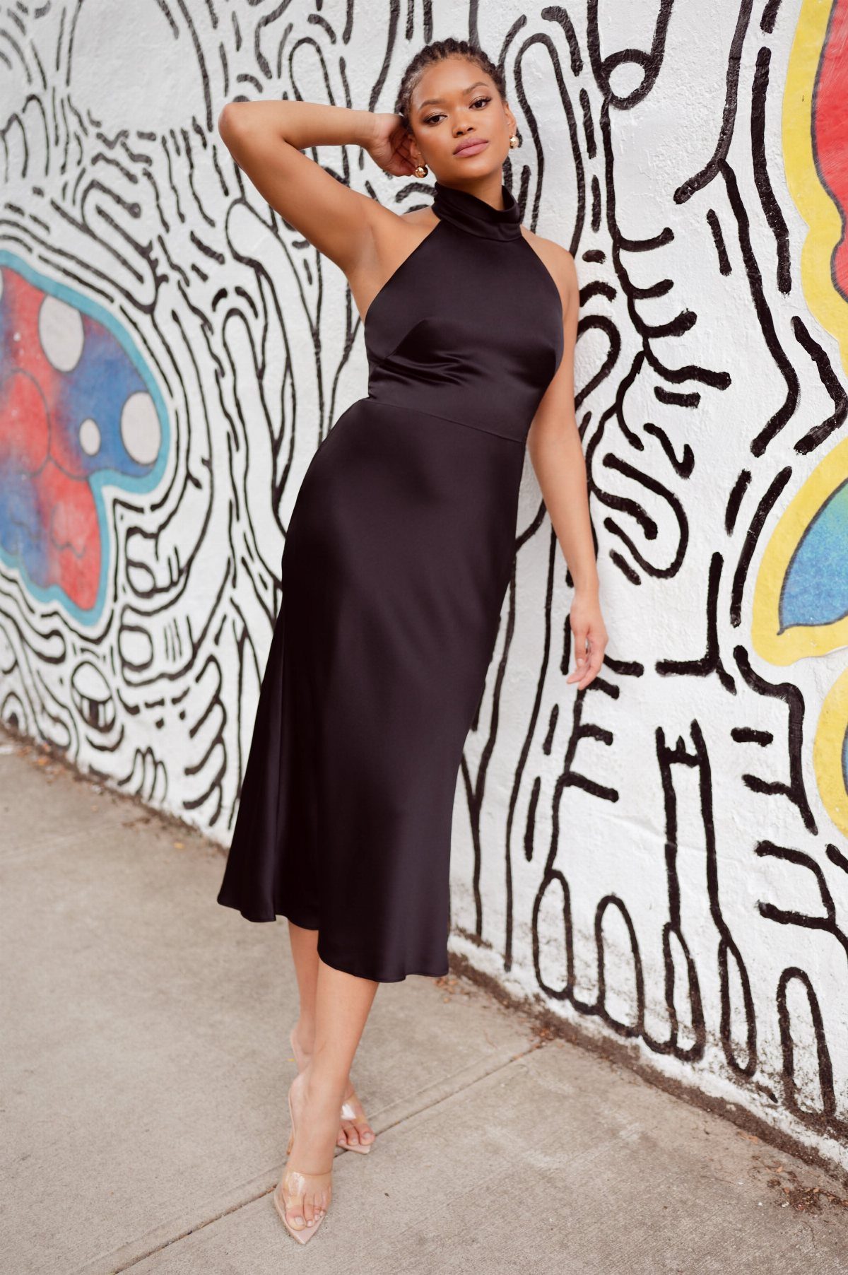 Woman in a black satin midi dress posing against a graffiti wall