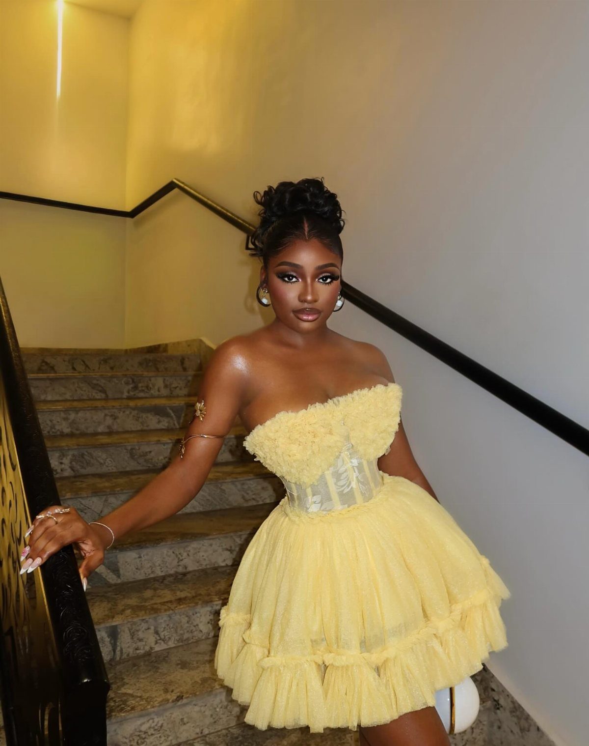 Woman in a yellow strapless corset top and tiered tulle mini skirt on stairs