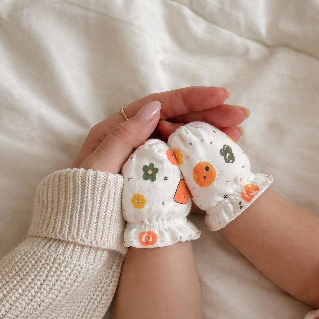 Baby hands wearing white floral patterned scratch mittens held by an adult hand