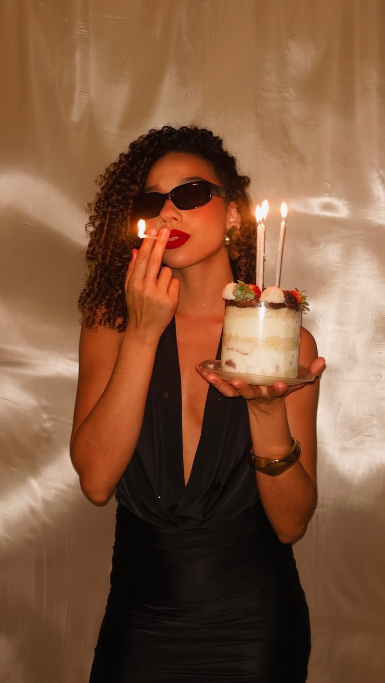 Woman in a plunging black dress holding a birthday cake with lit candles.