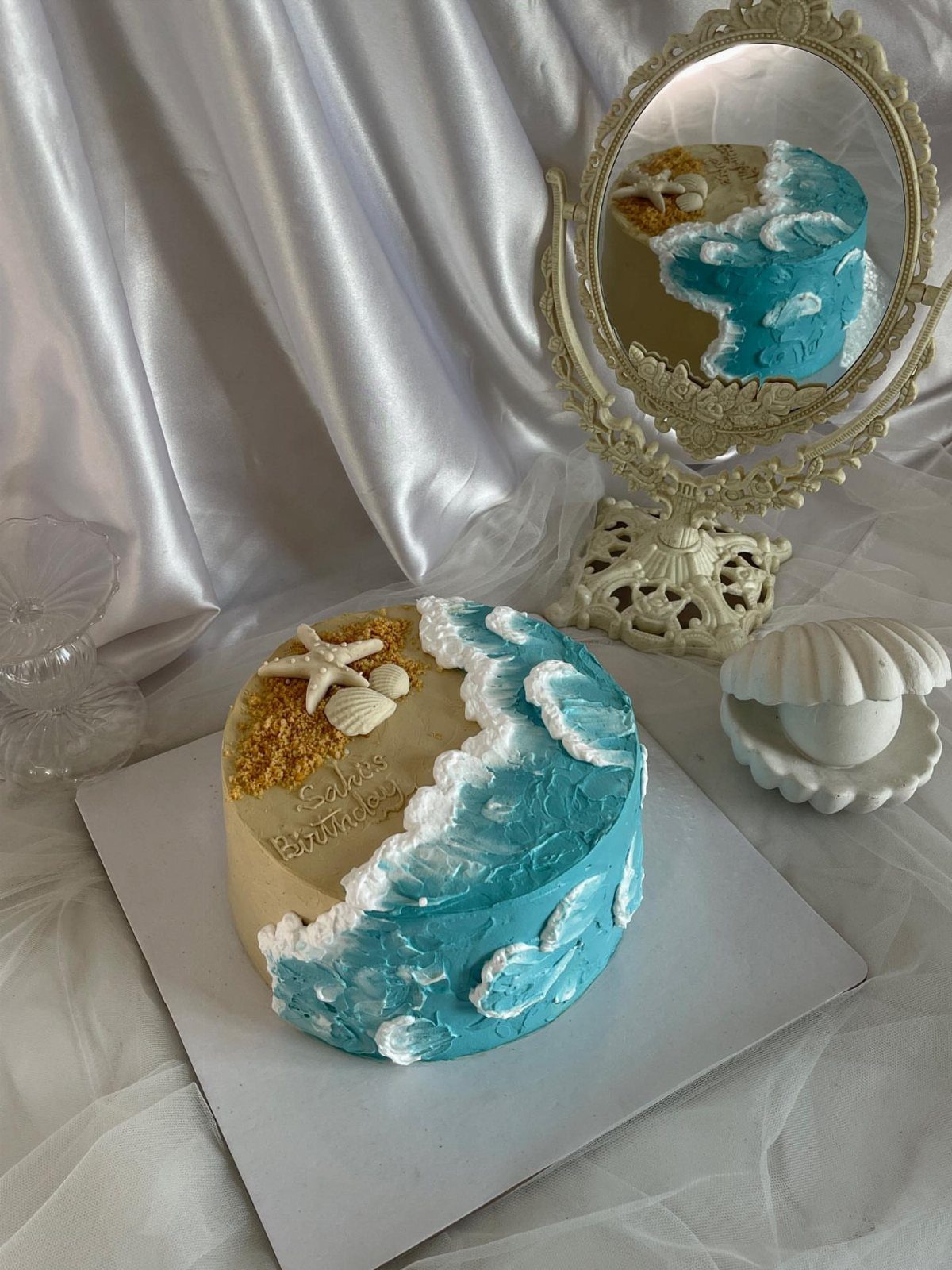 Beach themed cake with blue ocean waves, tan sand, and edible seashells.
