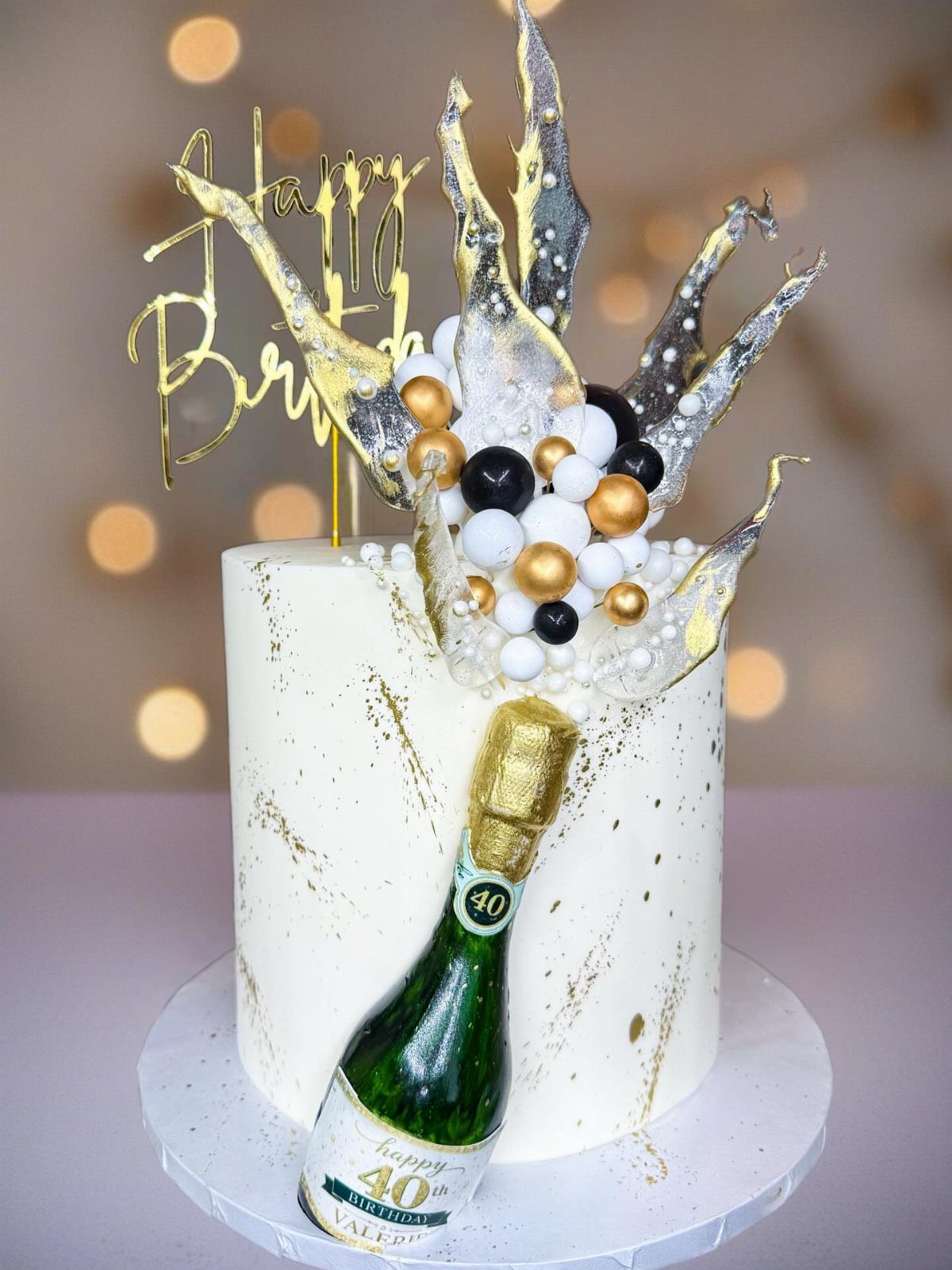 White birthday cake with a champagne bottle bursting out and gold decorations.