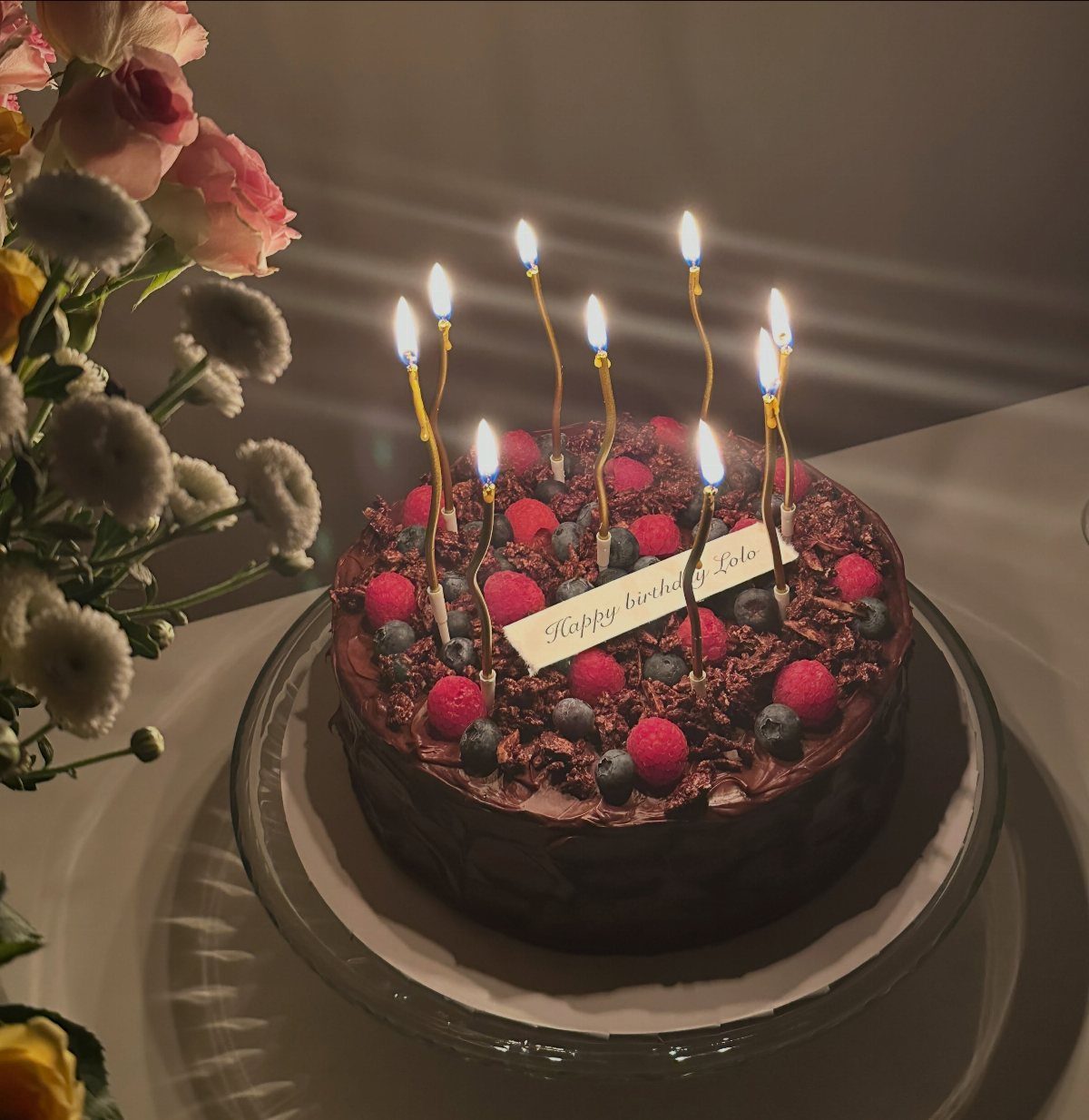 Chocolate birthday cake topped with fresh berries, chocolate shavings, and lit candles.