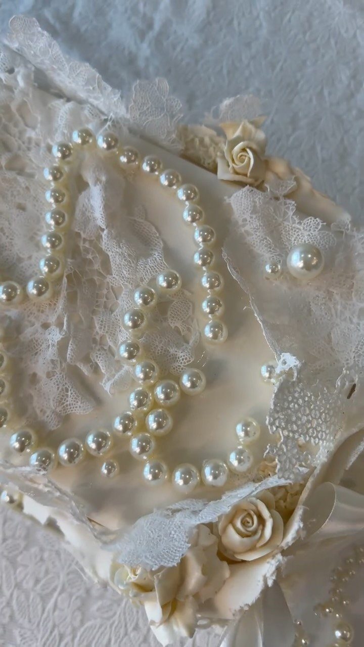 White frosted cake decorated with intricate lace patterns, pearl strings, and frosting roses.