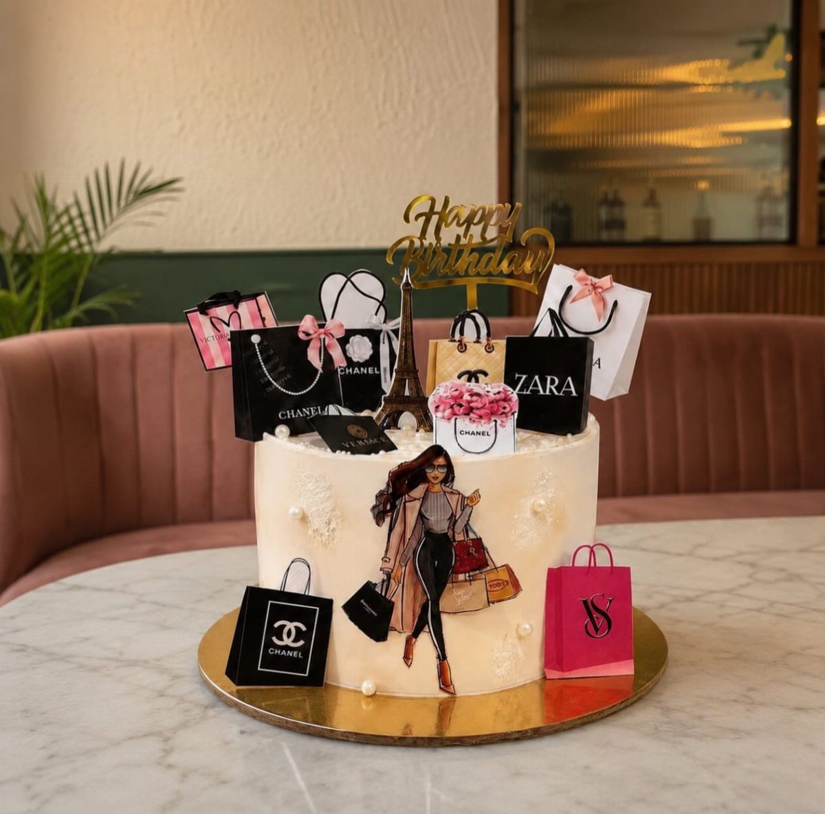 White birthday cake decorated with luxury shopping bags and a fashionable woman cutout.