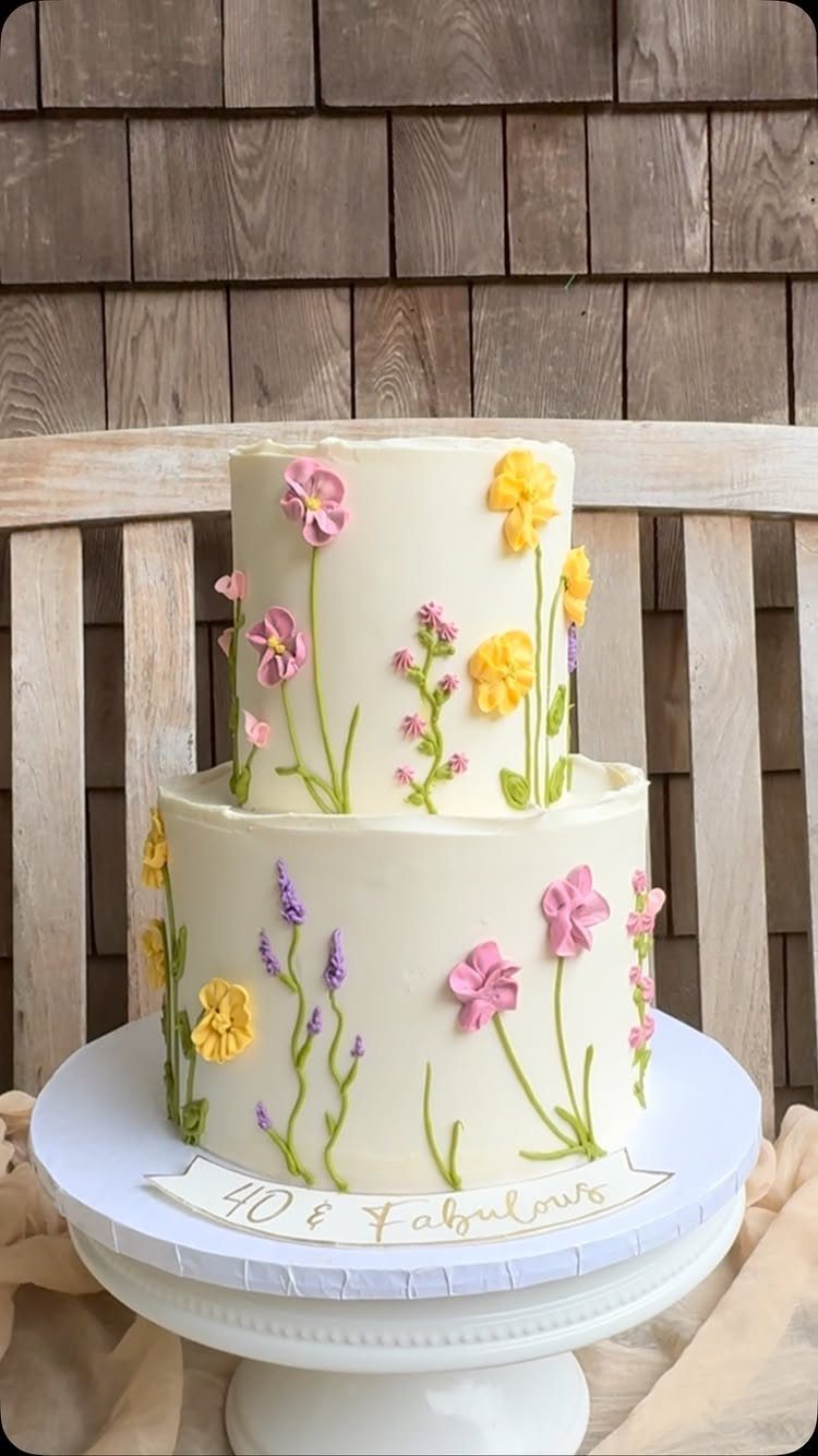 Two-tier white cake with colorful buttercream flowers and a 40 and Fabulous banner.
