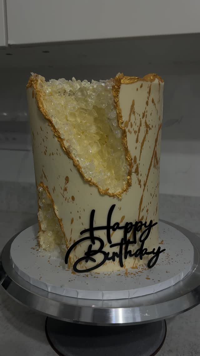 White birthday cake with a gold-edged geode cutout filled with amber edible crystals.