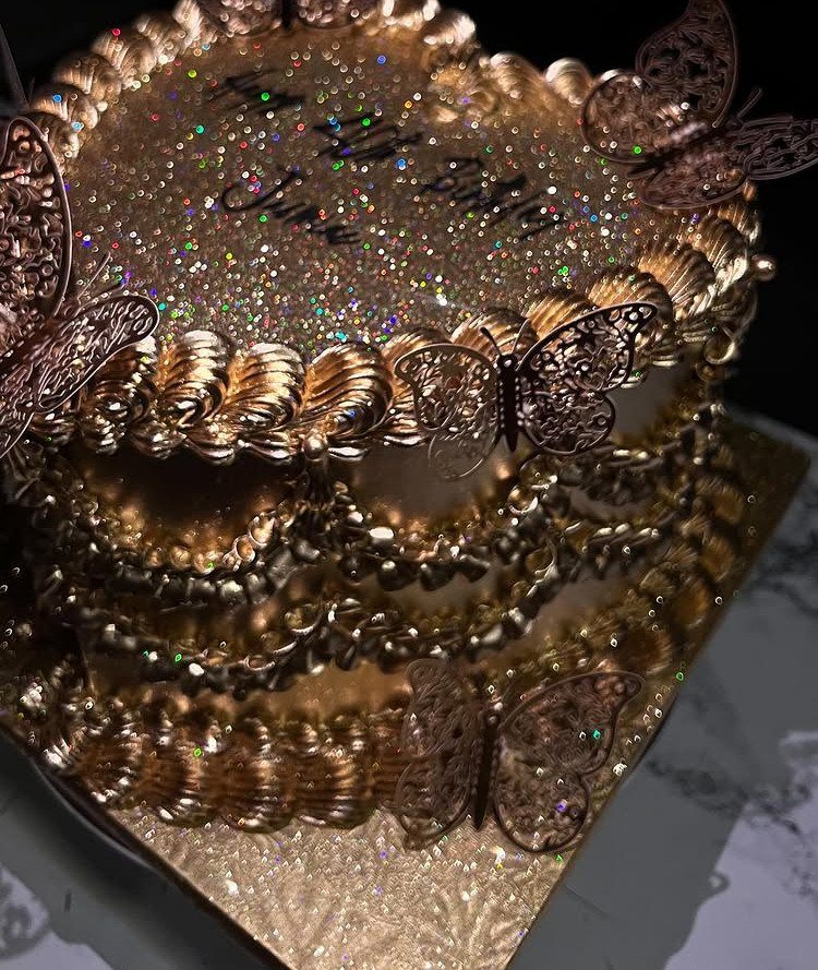 Gold glittery birthday cake decorated with gold frosting and metallic butterfly toppers.