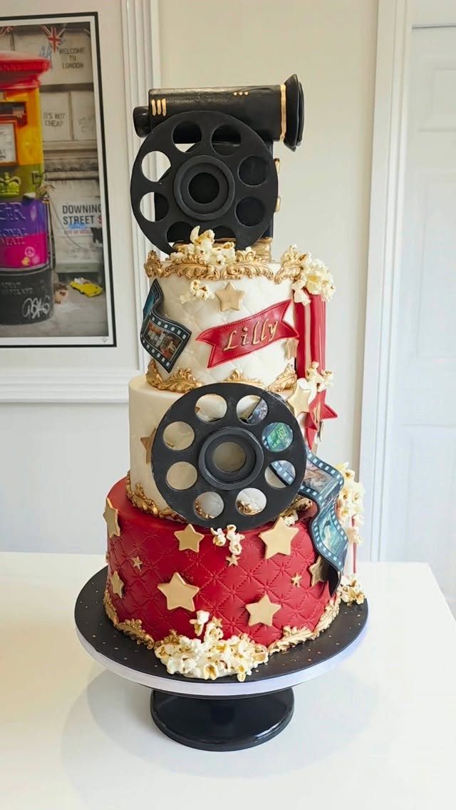 Three-tier movie themed cake with film reels, popcorn, and a movie camera topper.