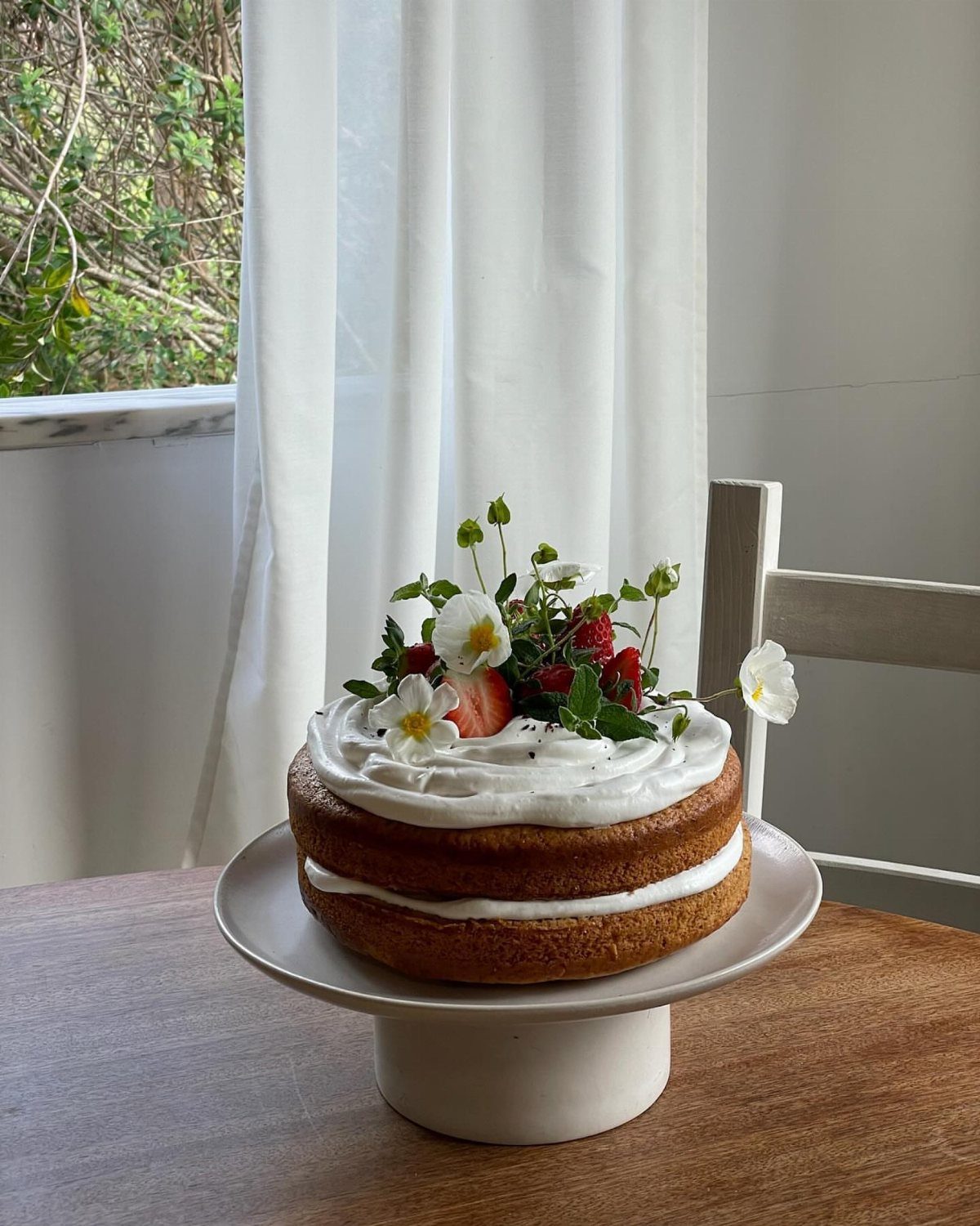 Two-layer naked sponge cake topped with white cream, strawberries, and delicate white flowers.