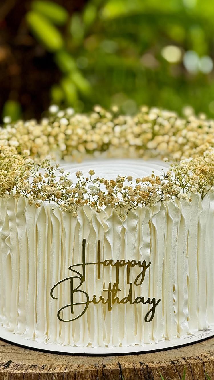 White ruffled birthday cake topped with baby's breath flowers and gold lettering