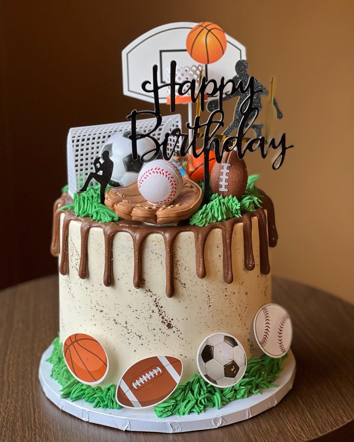 Sports themed birthday cake with chocolate drip and miniature athletic balls on top.