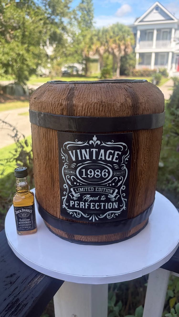 Whiskey barrel cake with vintage 1986 label and small whiskey bottle beside it.