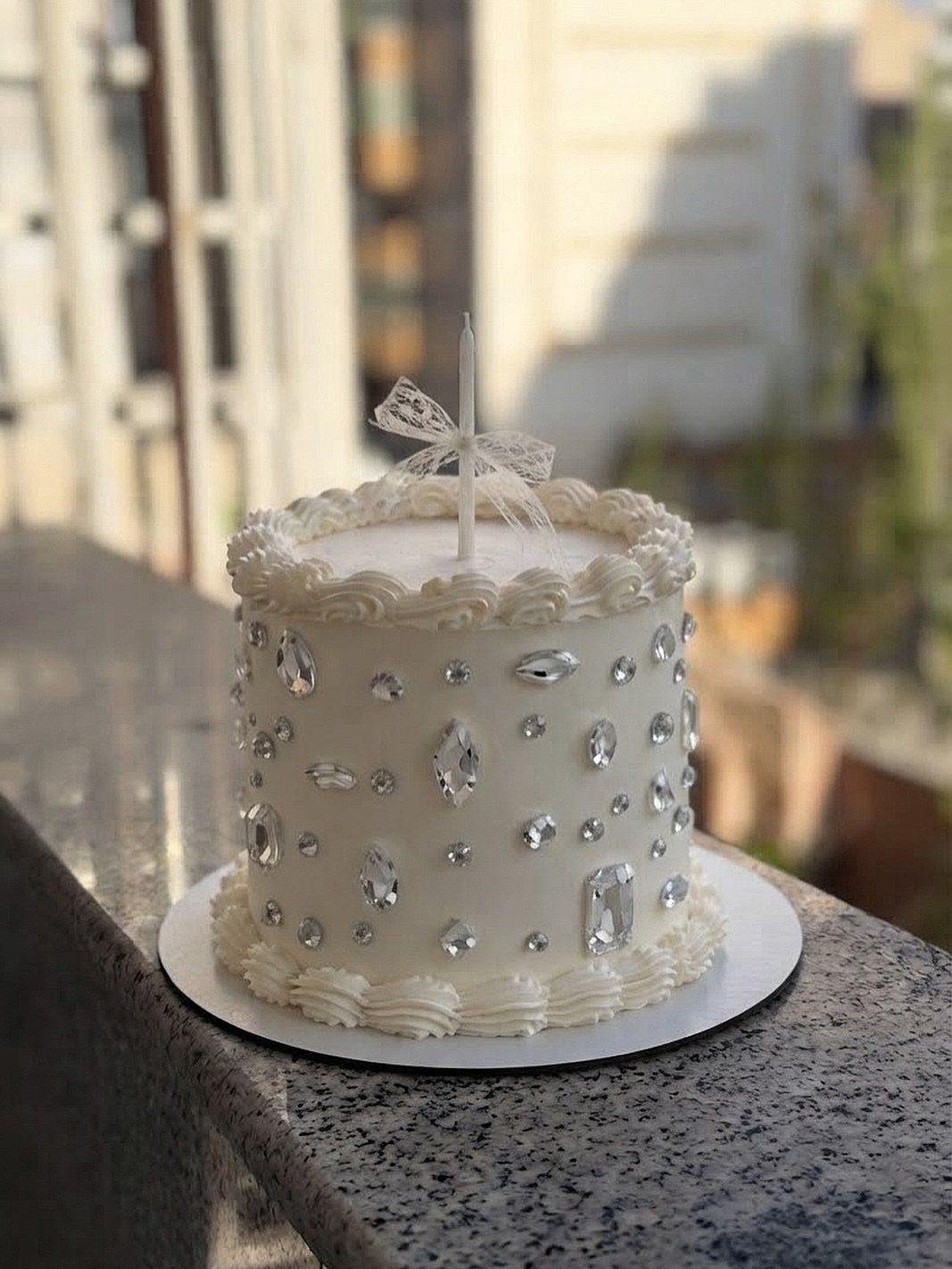 White frosted cake decorated with sparkling clear crystals and a single white candle.