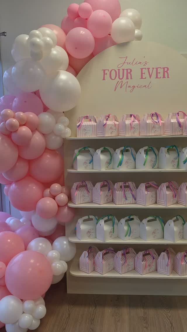 Pink and white balloon arch next to a magical themed birthday backdrop and treats.