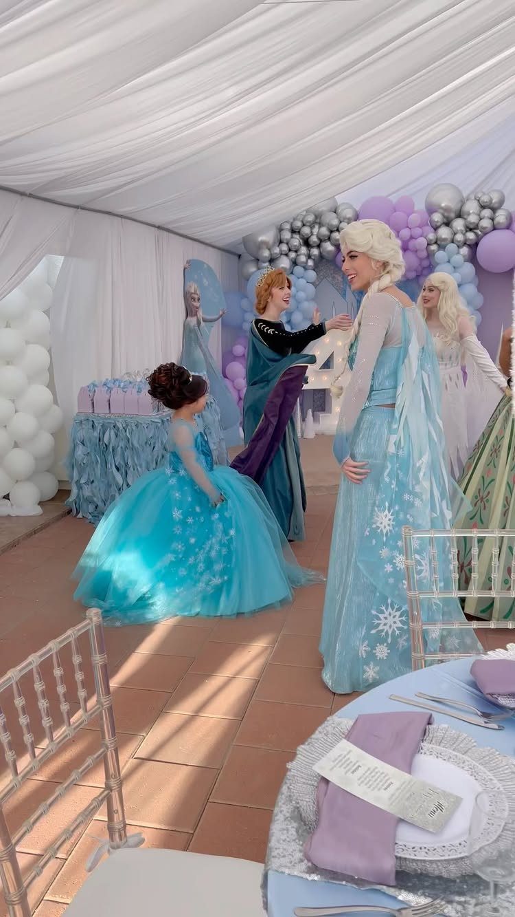 Frozen themed party with Elsa and Anna characters, blue balloons, and decorated tables.