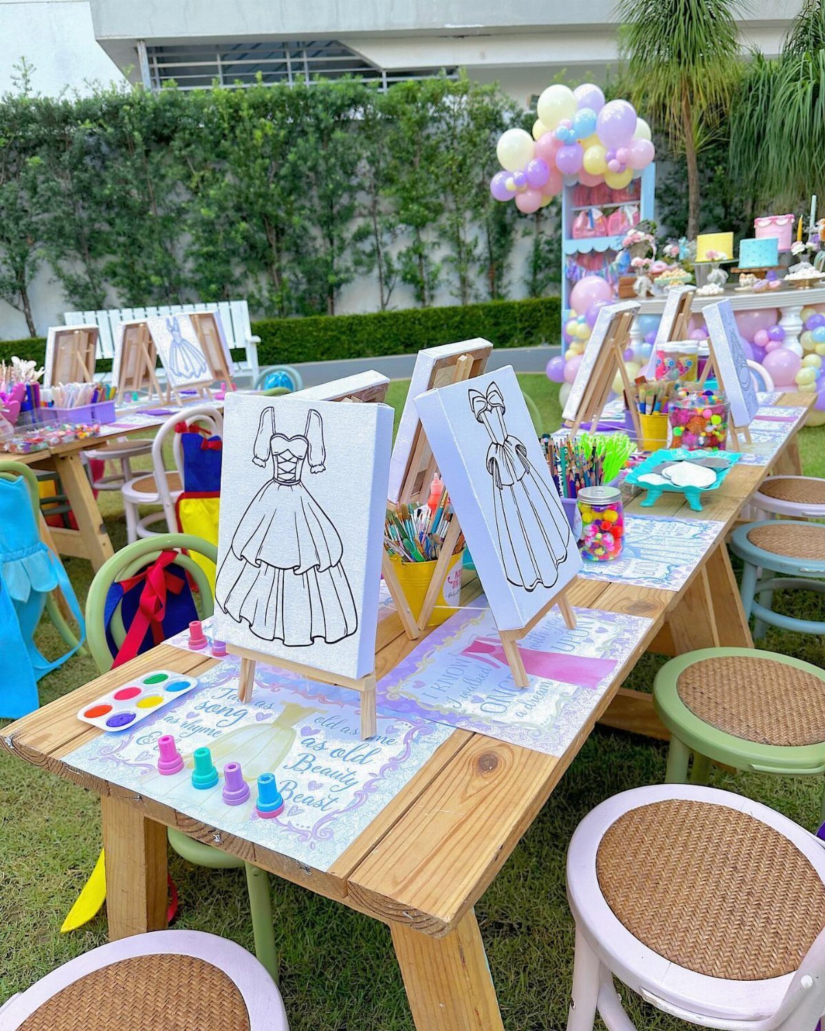 Outdoor painting station with ball gown canvases, colorful chairs, and pastel balloons.