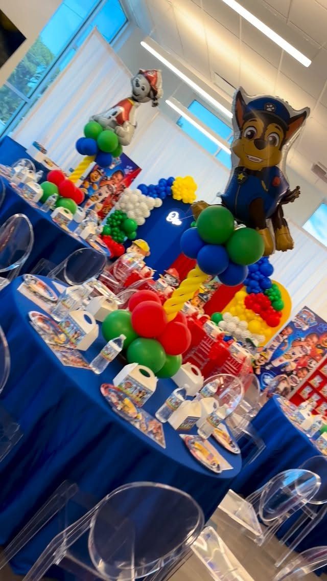 Paw Patrol party decorations with blue tablecloths, colorful balloons, and character balloons.
