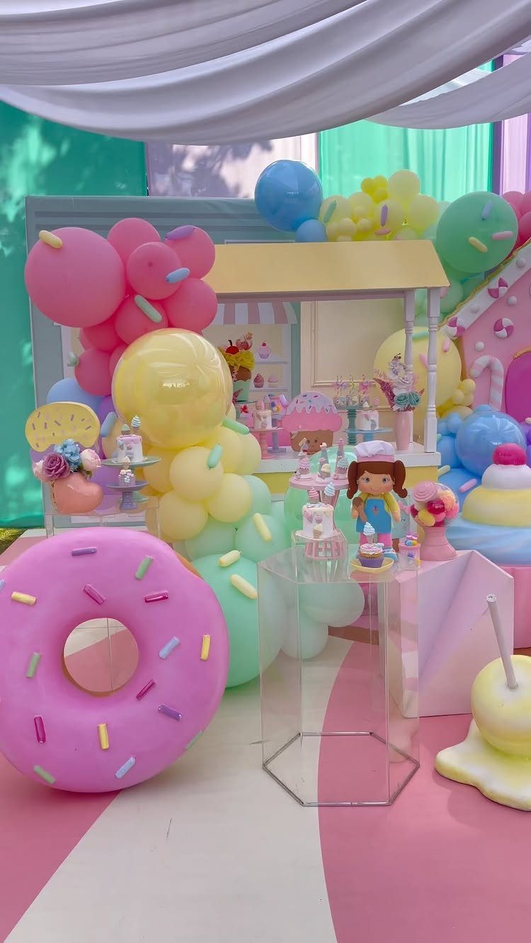 Whimsical candy land party setup with pastel balloons and a giant pink donut.