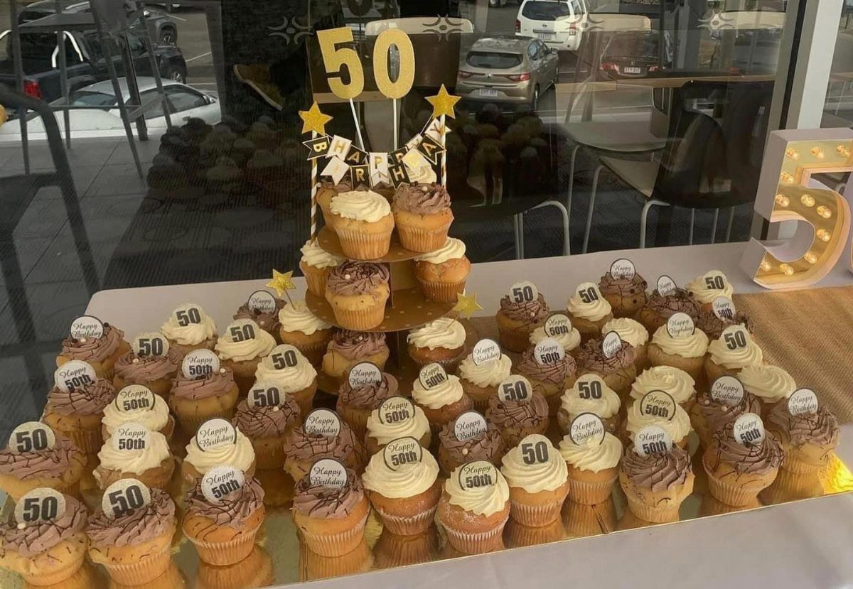 Many cupcakes with frosting and gold 50 toppers arranged for a birthday party.