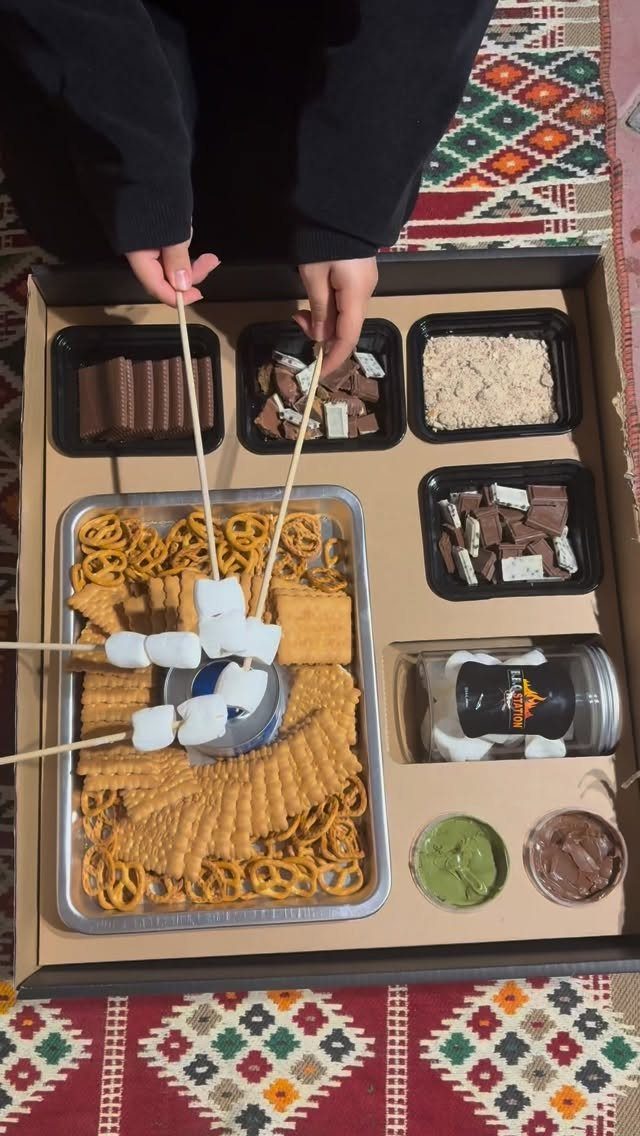 S'mores kit with graham crackers, chocolate, and marshmallows on skewers over a burner.