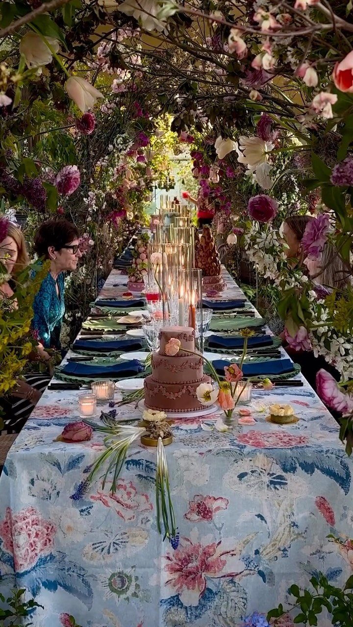 Long dining table with floral linens and cake under a flowering garden canopy