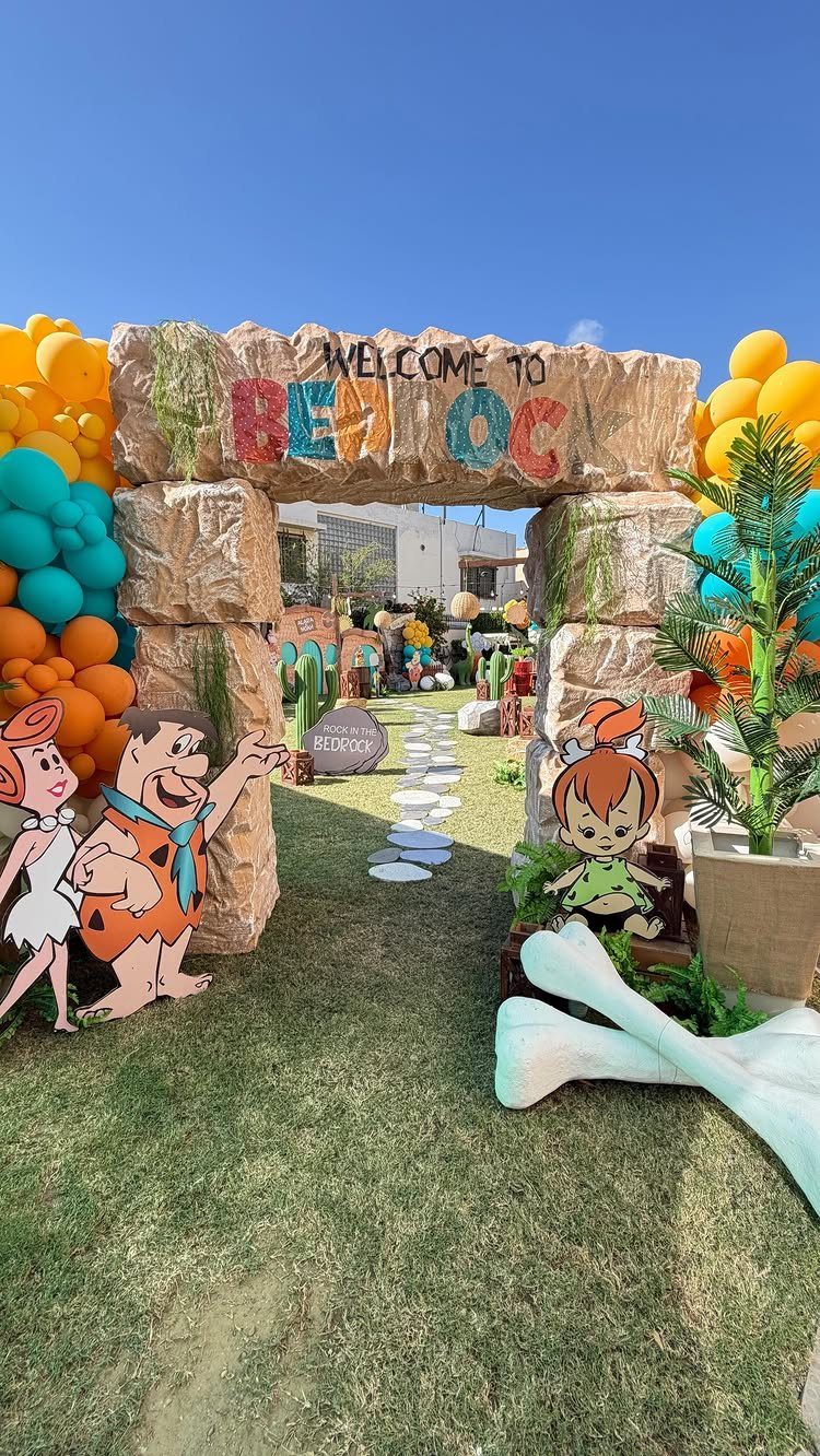 Stone archway entrance with Flintstones characters and colorful balloons for a themed party.