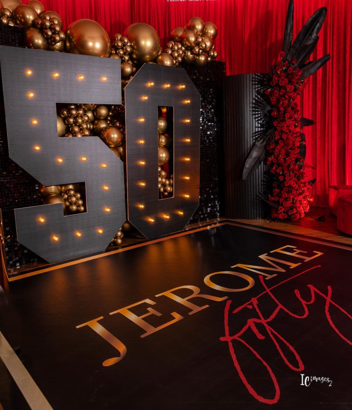 Large illuminated number 50 with gold balloons and red curtains for a party.